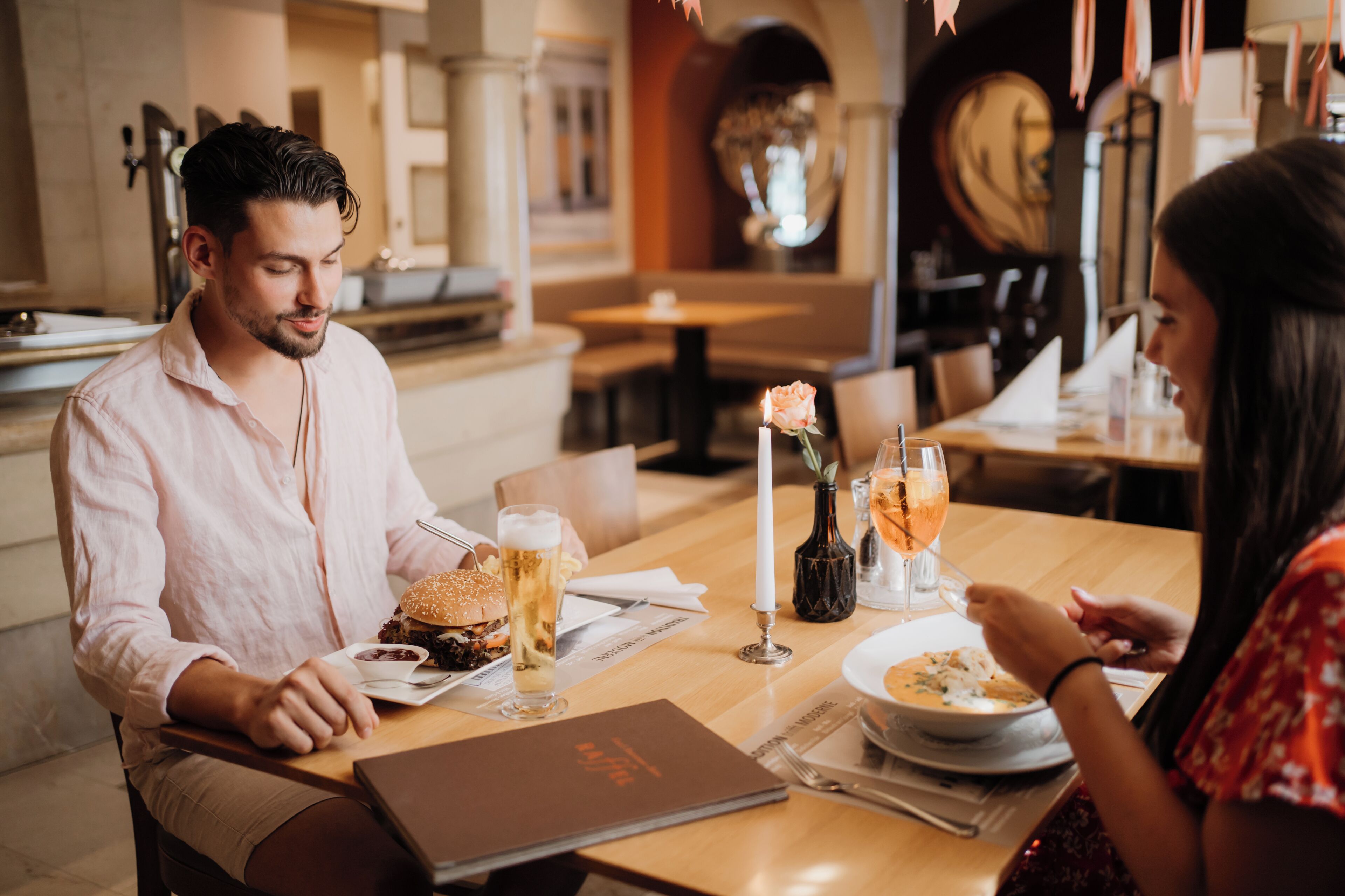 A restaurant setting with a wooden table, a menu, and a candle centerpiece.