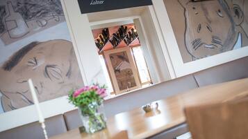 A dining area with a wooden table, a vase with flowers, and a wall with large abstract drawings.