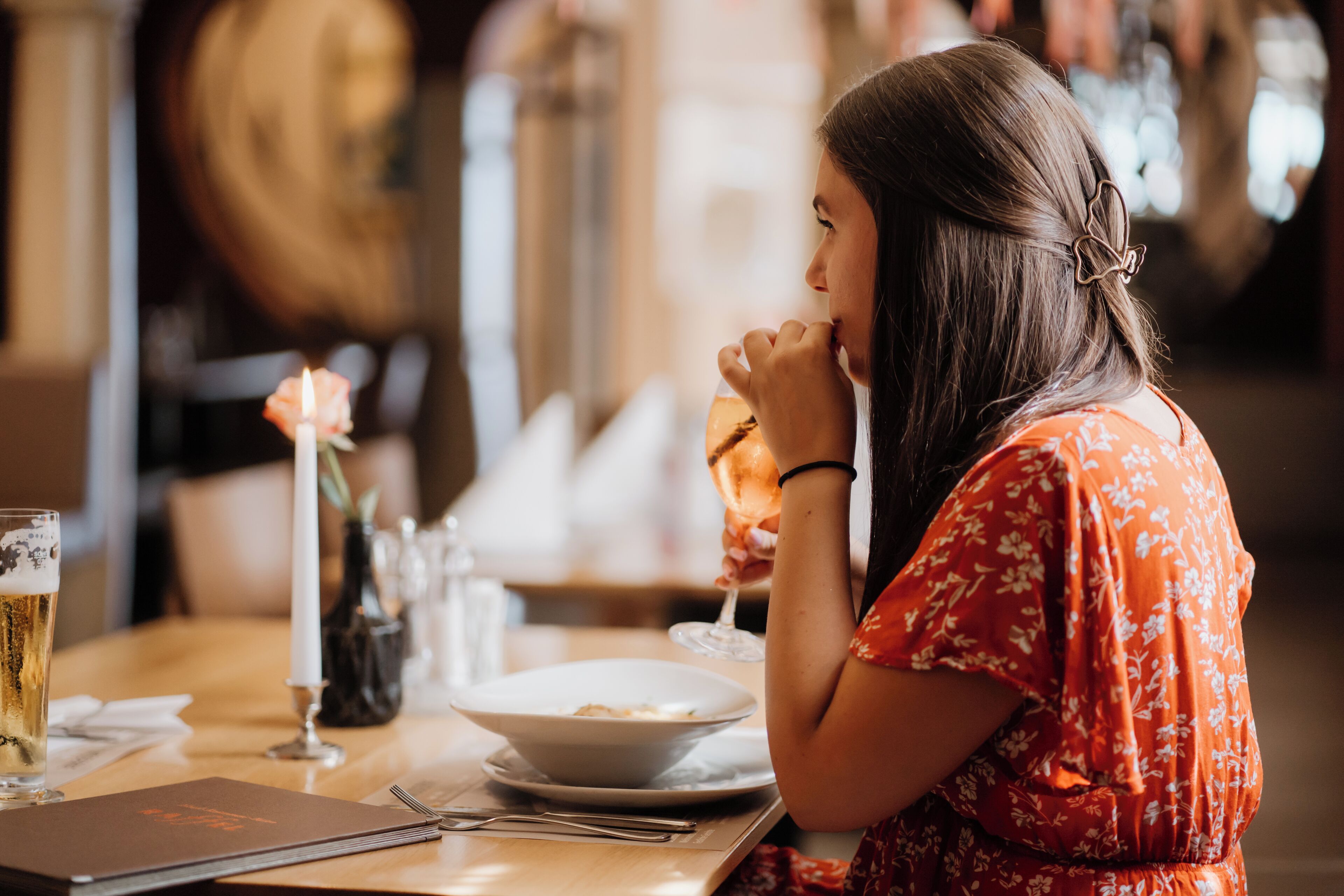 A person sitting at a table with a bowl, a glass of beer, and a menu.