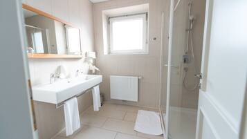 A modern bathroom with a double sink, a mirror, a window, a shower, and a radiator.