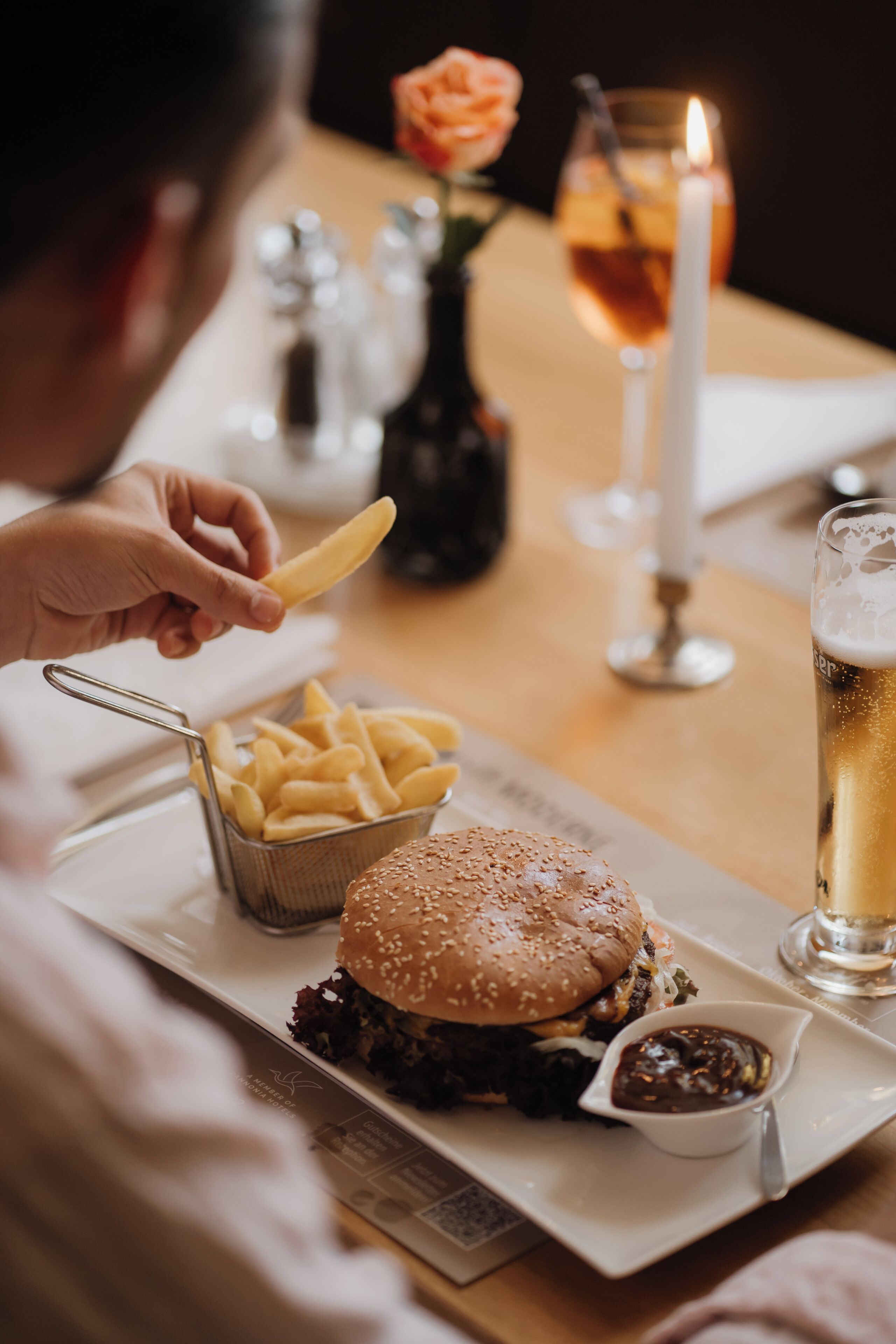 Una comida con una hamburguesa, papas fritas y una cerveza en una mesa.