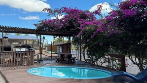 A wooden deck with a pool, picnic table, and barbecue grill.