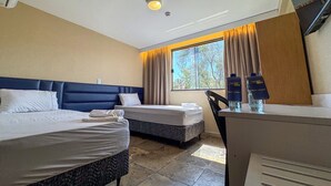 A hotel room with two beds, a desk, and a window with curtains.