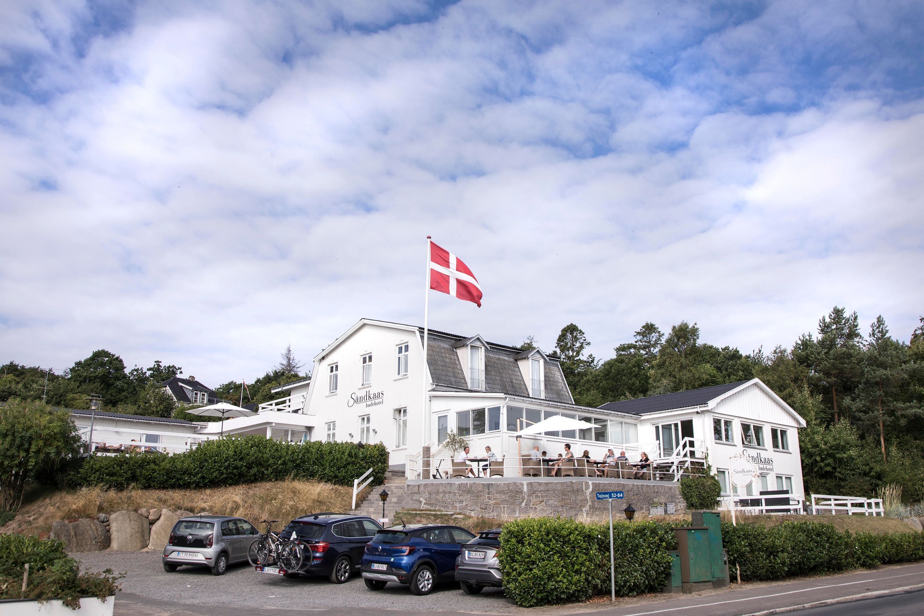 A white building with a flag, a staircase, and parked cars.
