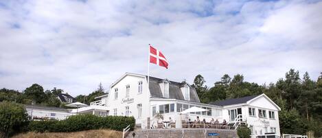A white building with a flag, a staircase, and parked cars.