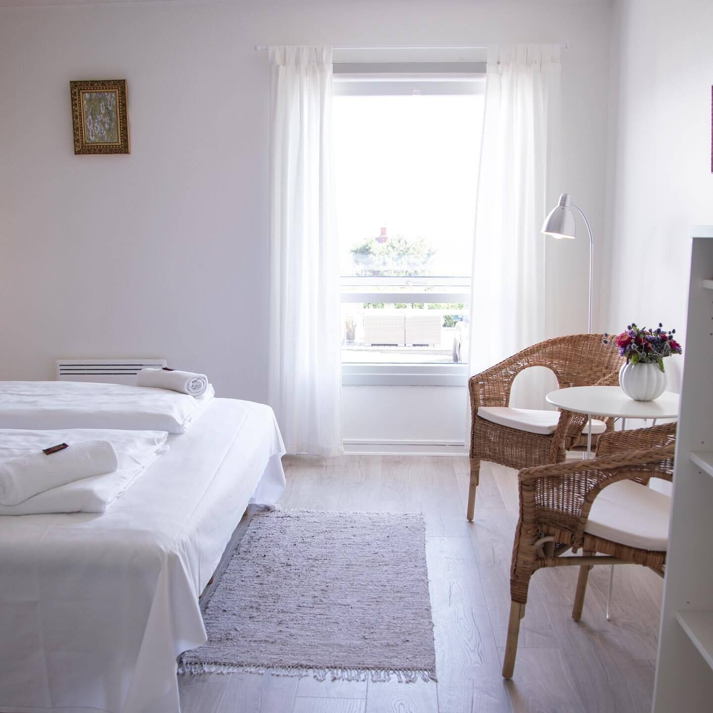 Habitación de hotel con dos camas, una silla de mimbre, una mesita y vista al exterior.
