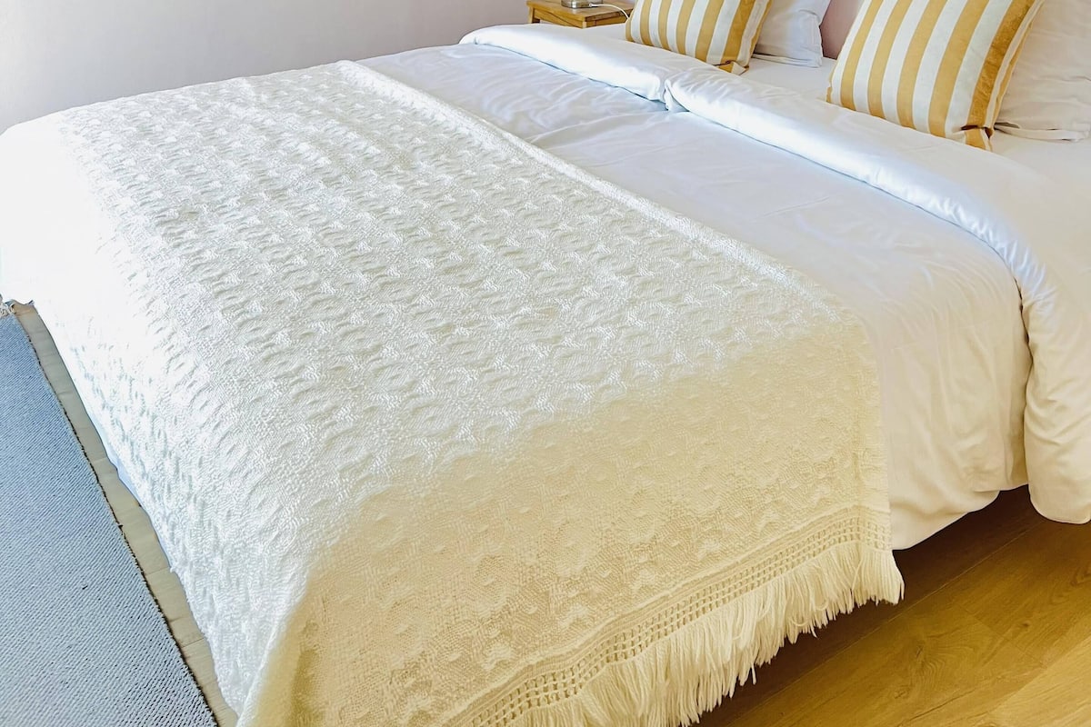 A neatly made bed with white linens, a bedside lamp, and striped pillows.