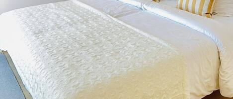 Una cama bien hecha con sábanas blancas, una lámpara de noche y almohadas a rayas.
