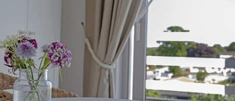 On voit clairement un balcon avec une balustrade blanche, une chaise en osier et un vase rempli de fleurs posé sur une table.
