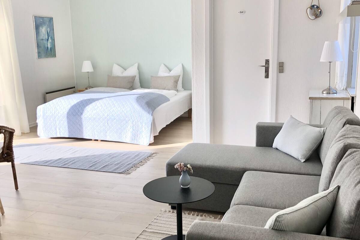 A modern hotel room with a bed, a sofa, a small table, and a door.