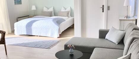 A modern hotel room with a bed, a sofa, a small table, and a door.