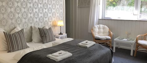 Habitación de hotel con una cama grande, dos mesitas de noche, una silla y una ventana con vistas a zonas verdes.