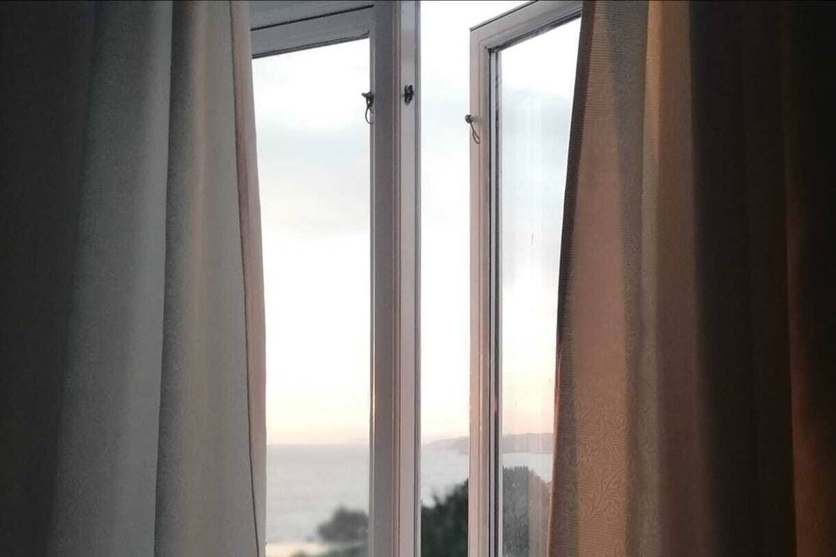 A window with curtains partially drawn, revealing a view of a cityscape and a body of water.