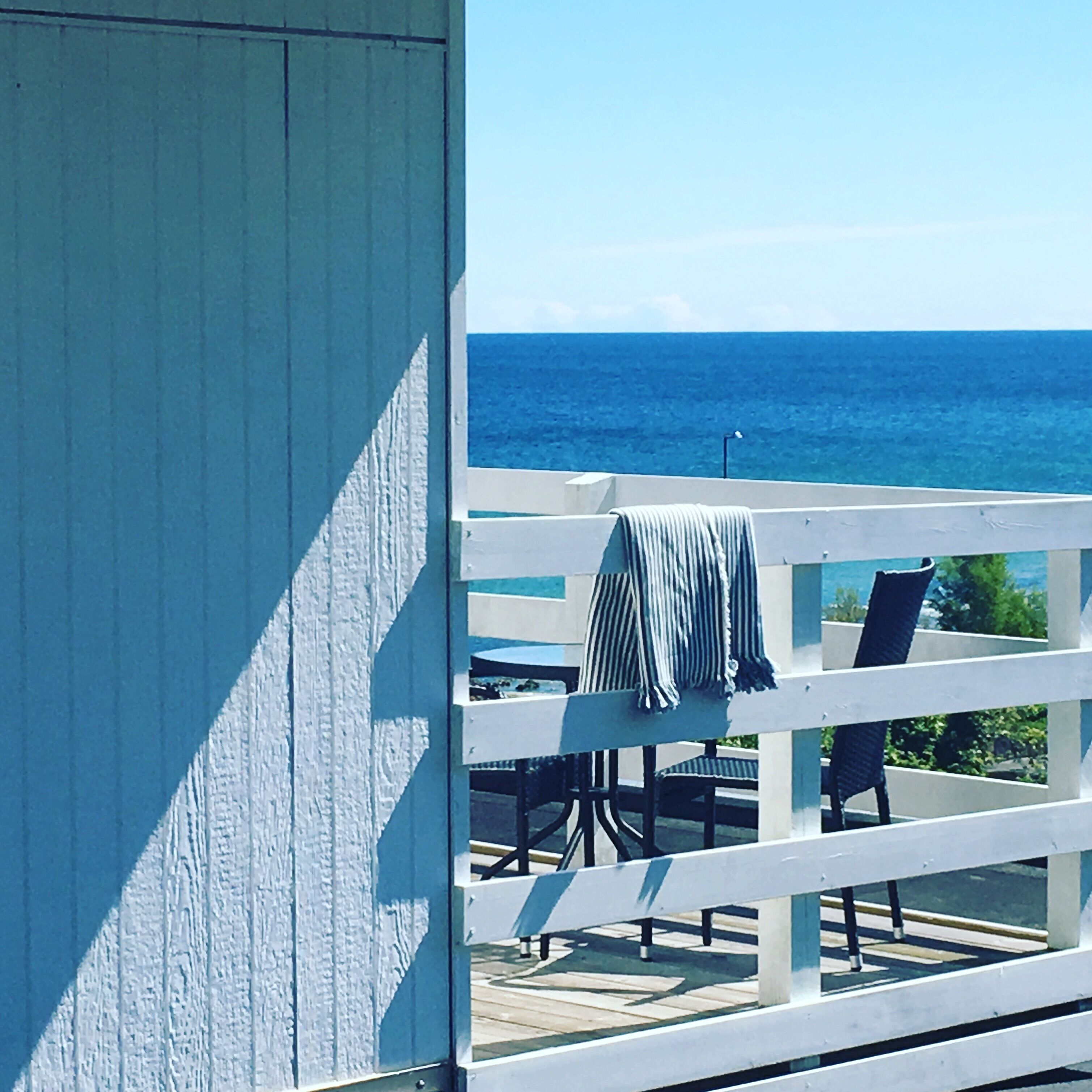 Une terrasse avec vue sur l’océan, une balustrade blanche et une chaise sur laquelle est posée une serviette à rayures.
