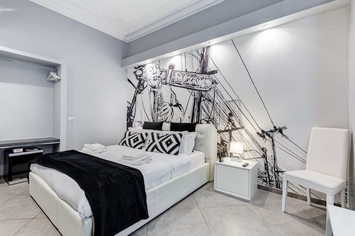 A modern bedroom with a bed, bedside tables, a chair, and a wall mural.