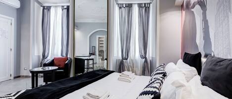 Une chambre d’hôtel moderne avec un grand lit, un coin salon comprenant une chaise et une table, ainsi qu’un miroir.