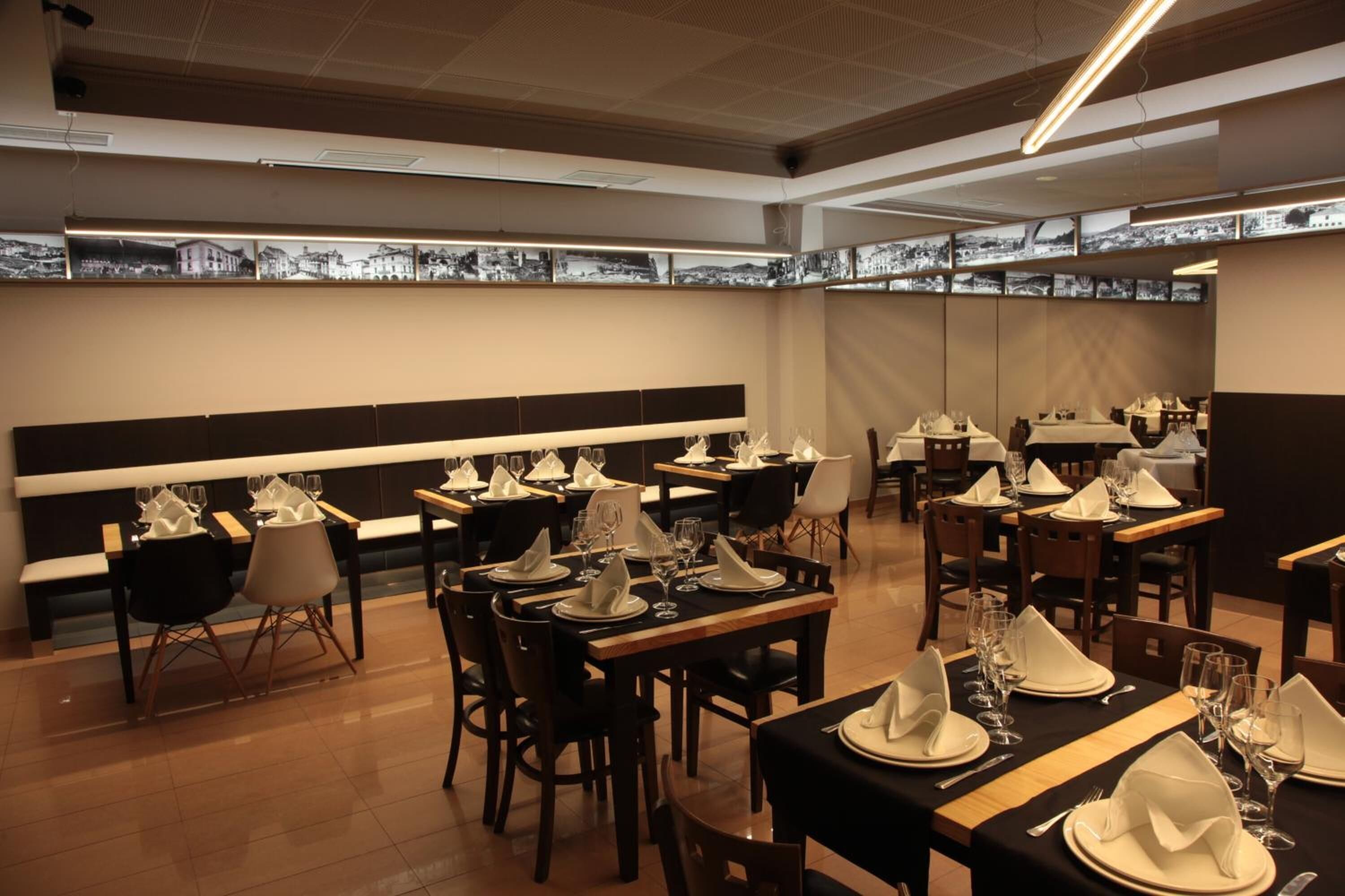 Un restaurant amb diverses taules preparades per dinar, amb un interior modern que destaca el terra de fusta i decoració mural en blanc i negre.