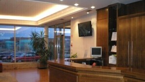 Un área de recepción con mostrador de madera, un televisor montado en la pared y un ventanal grande con vista a un estacionamiento.