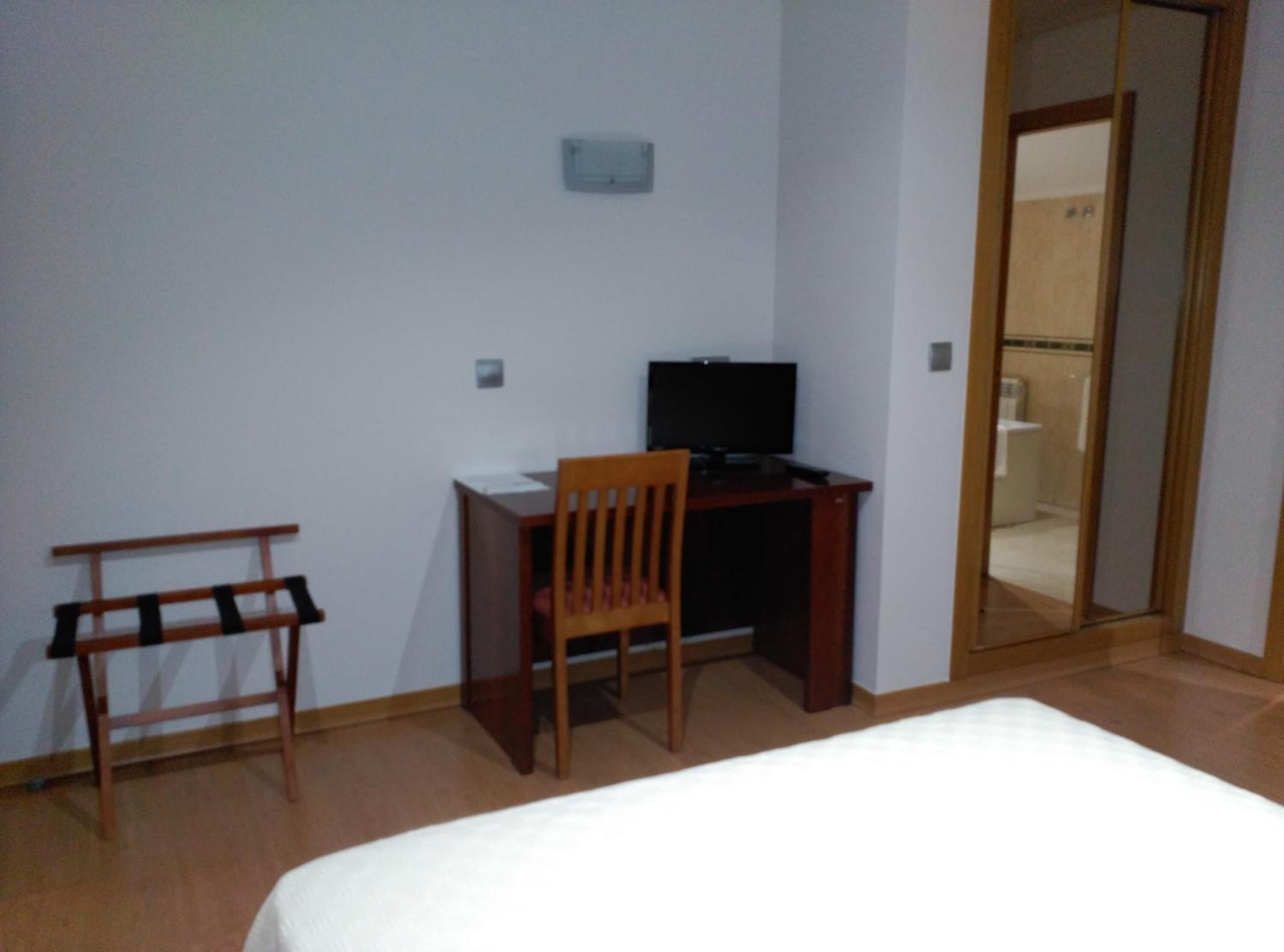 Un dormitorio con cama, escritorio con silla, televisor y espejo.