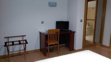 Un dormitorio con cama, escritorio con silla, televisor y espejo.