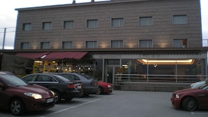 Un hotel de varios pisos con fachada plana, un restaurante a nivel de calle y varios coches aparcados en el estacionamiento.