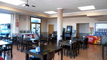 L’intérieur d’un restaurant, avec plusieurs tables et chaises, une caisse enregistreuse et un distributeur automatique.
