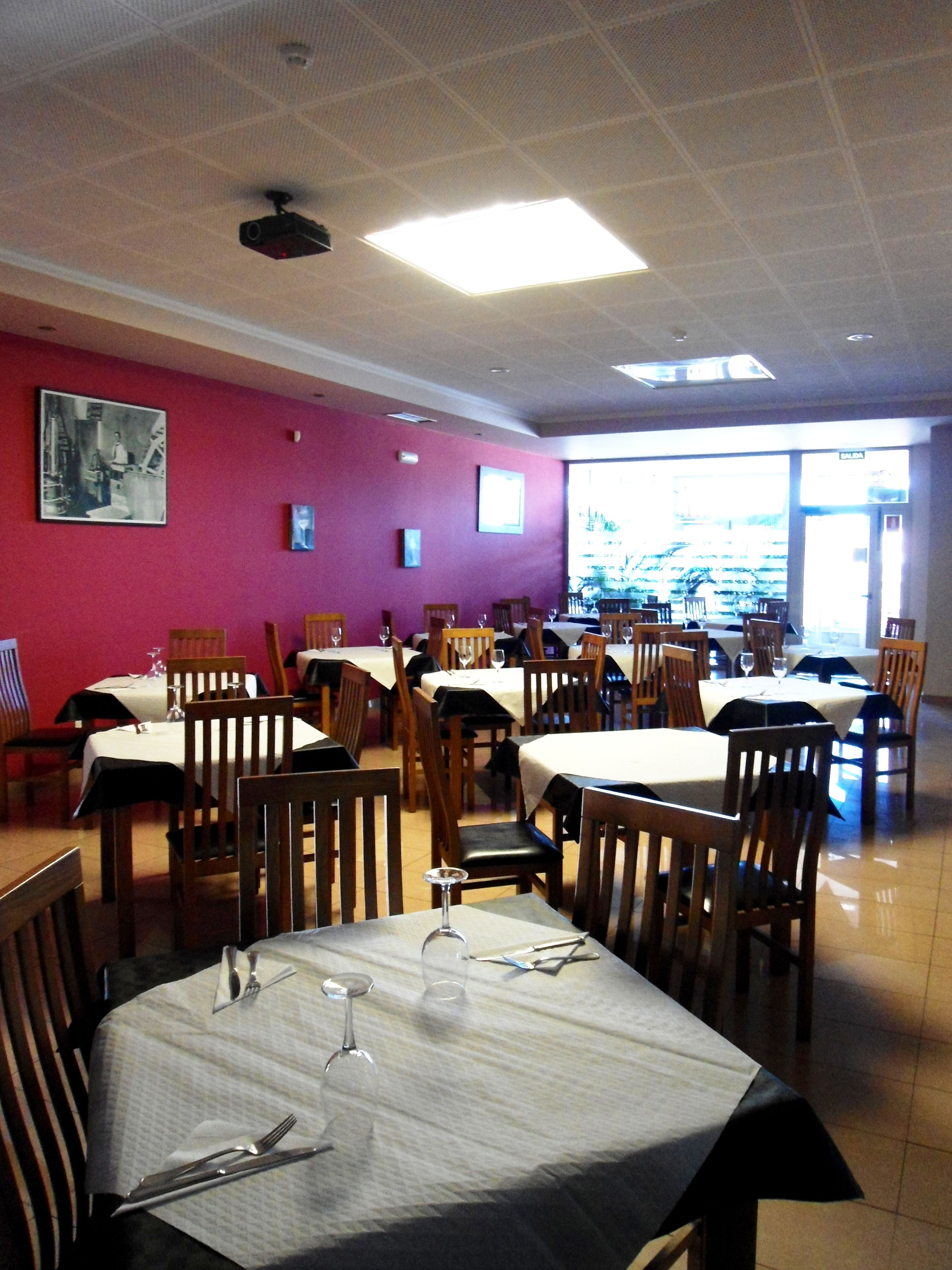 Ein Restaurant mit mehreren Tischen und Stühlen, einer roten Wand mit gerahmten Bildern und einem großen Fenster mit Blick nach draußen.