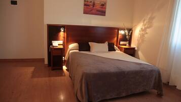 A bedroom with a large bed, two bedside tables, a nightstand, a wall-mounted lamp, and a painting on the wall.