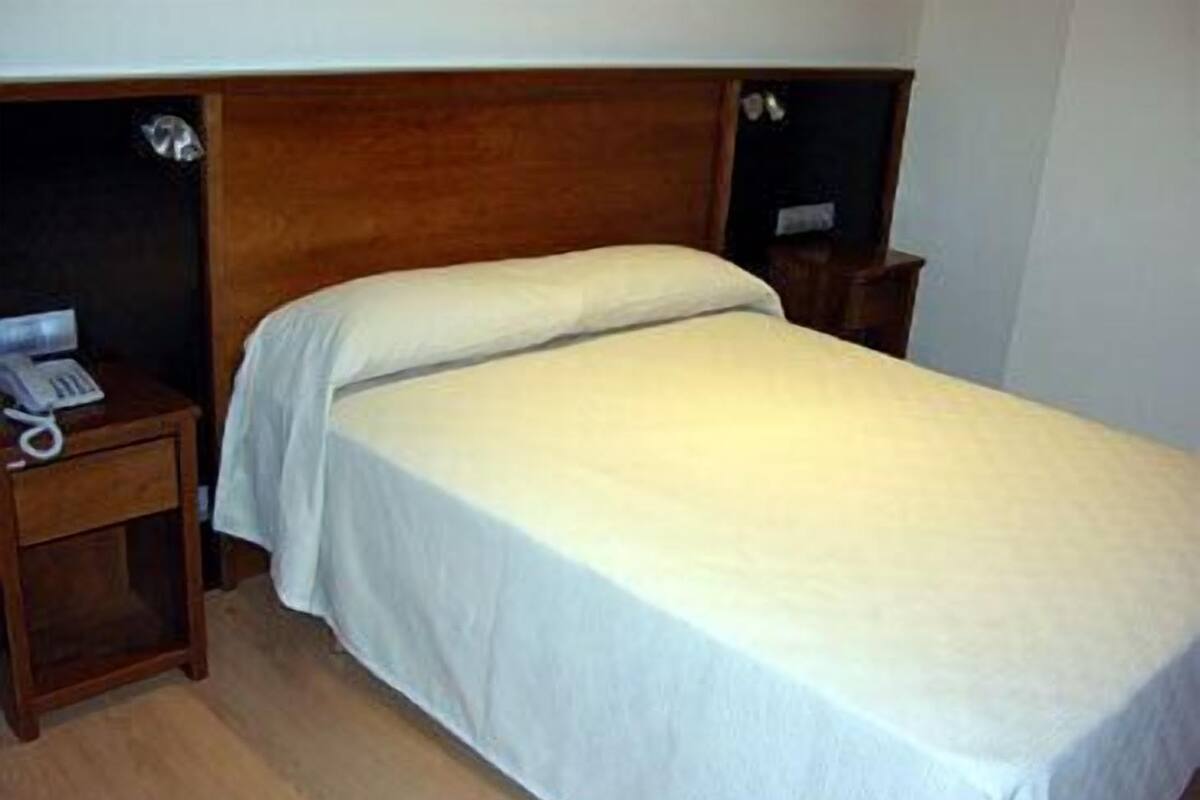 Una cama individual con cabecera de madera y una mesita de noche con teléfono.