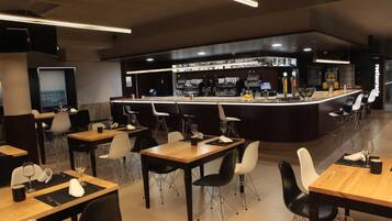 Un restaurante moderno con una zona de bar, varias mesas con sillas y un mostrador con la carta.