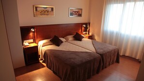 Una cama doble con cabecera de madera, dos mesitas de noche con lámparas y dos cuadros colgados en la pared.
