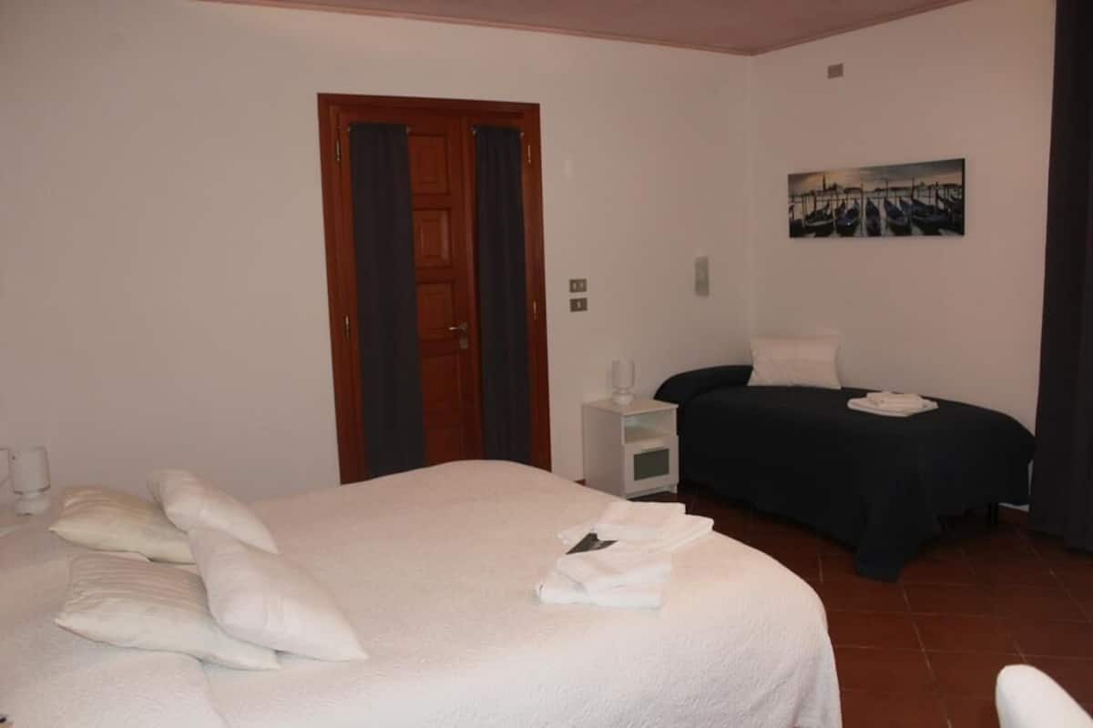 A hotel room with a large bed, a smaller bed, a nightstand, a painting on the wall, and a door with curtains.