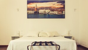 A hotel room with a bed, two bedside tables, a chair, and a cityscape painting on the wall. - Airport Venice Diego 2 (Mestre)