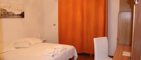 A hotel room with a bed, a chair, a shower area, and a curtain.