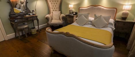 A bedroom with a large bed, a vanity with a mirror, a chair, and two bedside tables with lamps.
