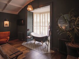 Un baño con una bañera independiente, suelo de madera, radiador y una planta en maceta.