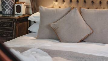 A bed with a tufted headboard, two pillows, and a bedside table with a lamp and a decorative vase.