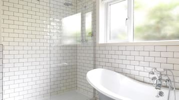 Un baño moderno con azulejos blancos tipo metro, una bañera independiente, un box de ducha de vidrio y una ventana que proporciona luz natural.