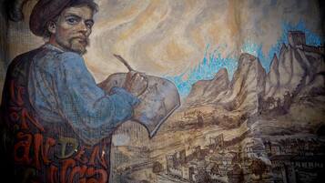 A mural of a person painting a landscape with mountains and a village.