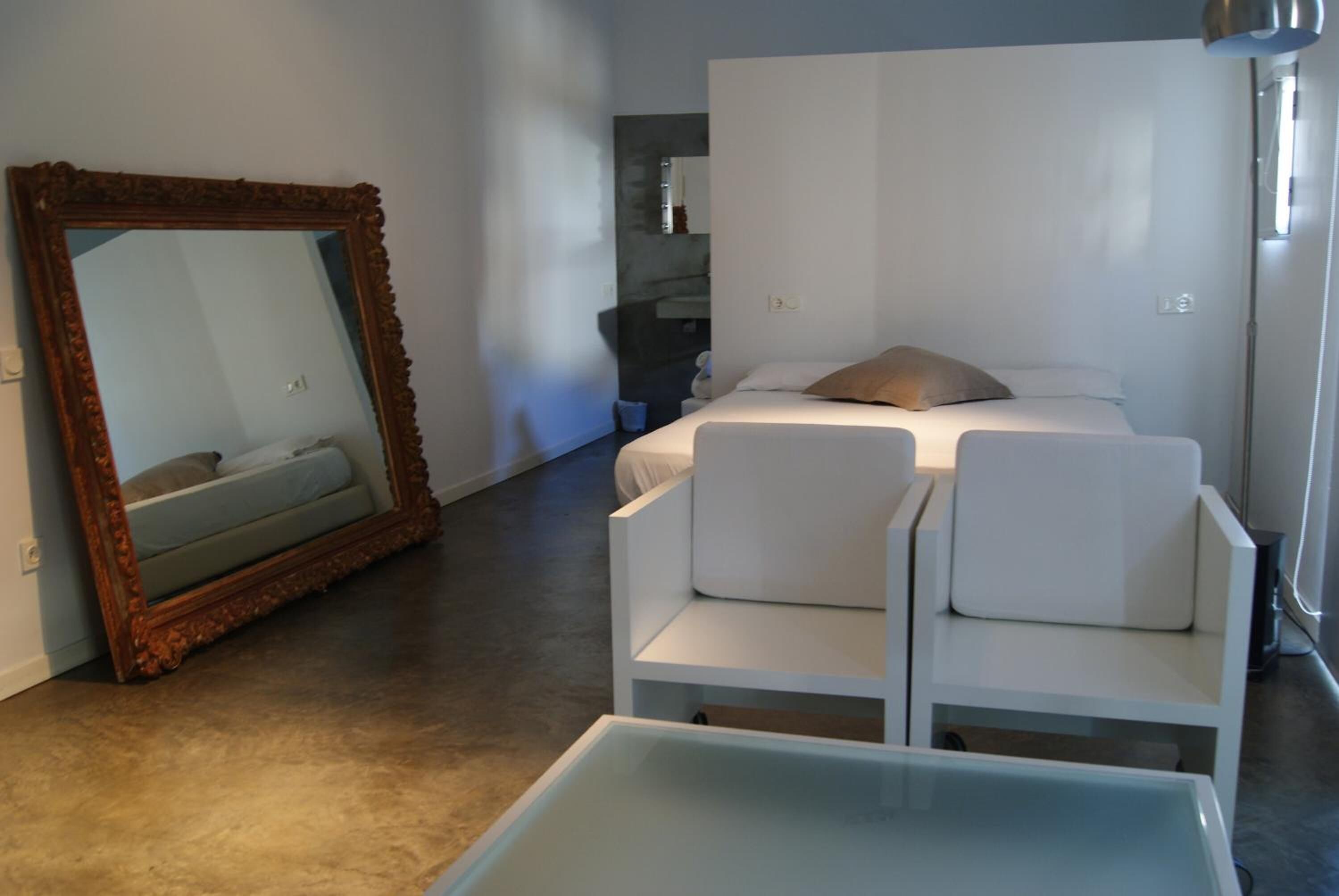 Un dormitorio moderno con un espejo grande, una cama con ropa blanca y una silla blanca.