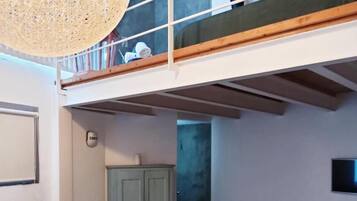 A modern loft-style room with a glass coffee table, a loft bed with a wooden frame, a green cabinet, and a hanging light fixture.