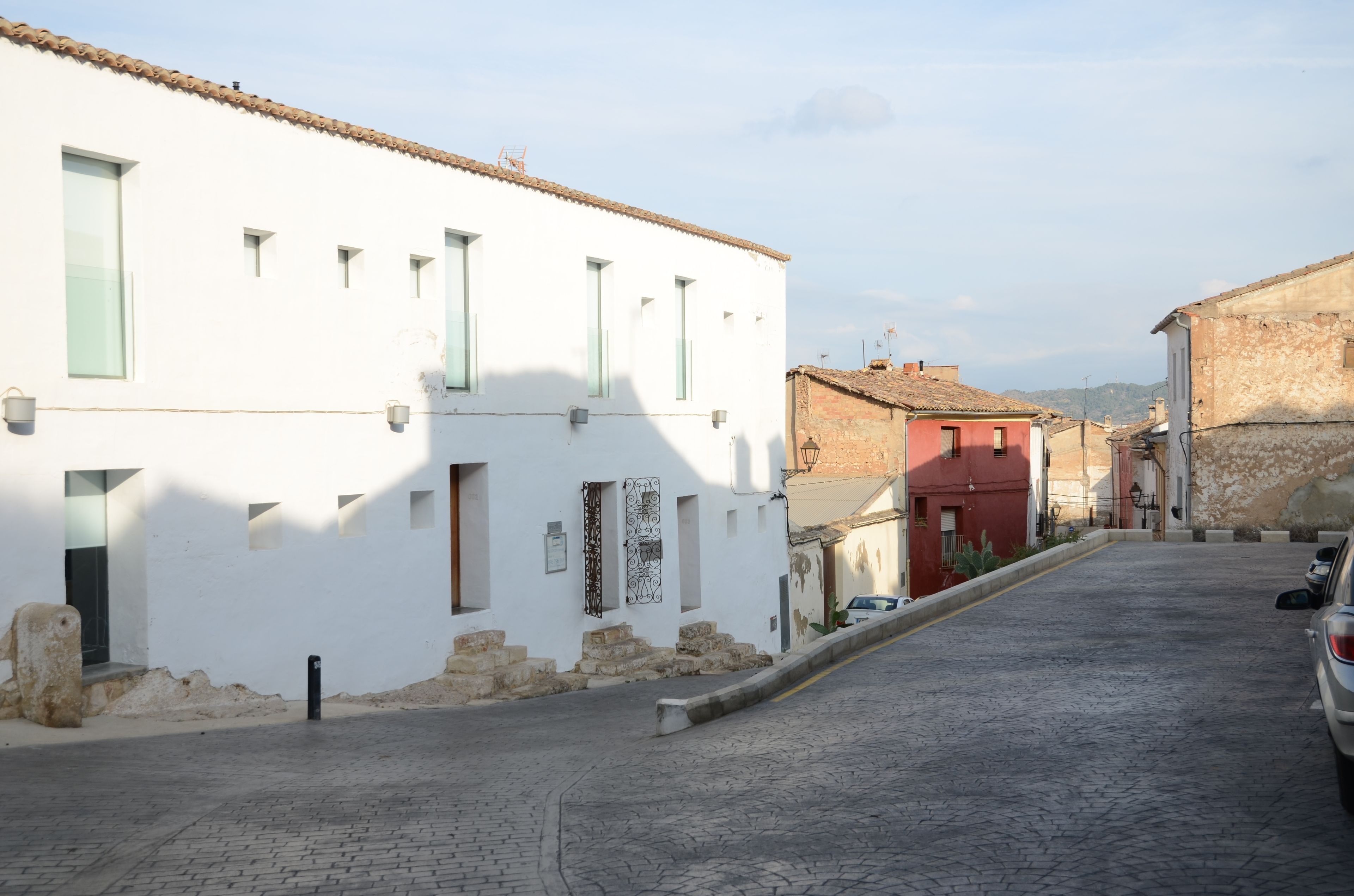 A narrow cobblestone street flanked by white and red buildings with small windows and doors.