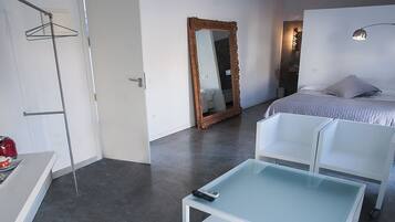 A bedroom with a bed, bedside table, mirror, and a hanging coat rack.