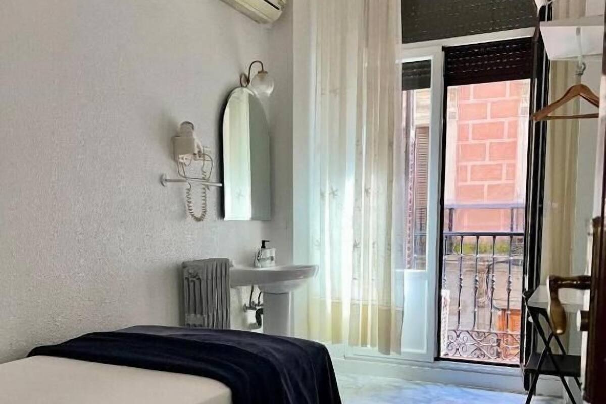 A hotel room with a bed, a sink, a mirror, and a balcony with a view of the outside.