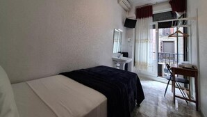 A bedroom with a bed, a desk, a chair, a window with curtains, and an air conditioning unit.
