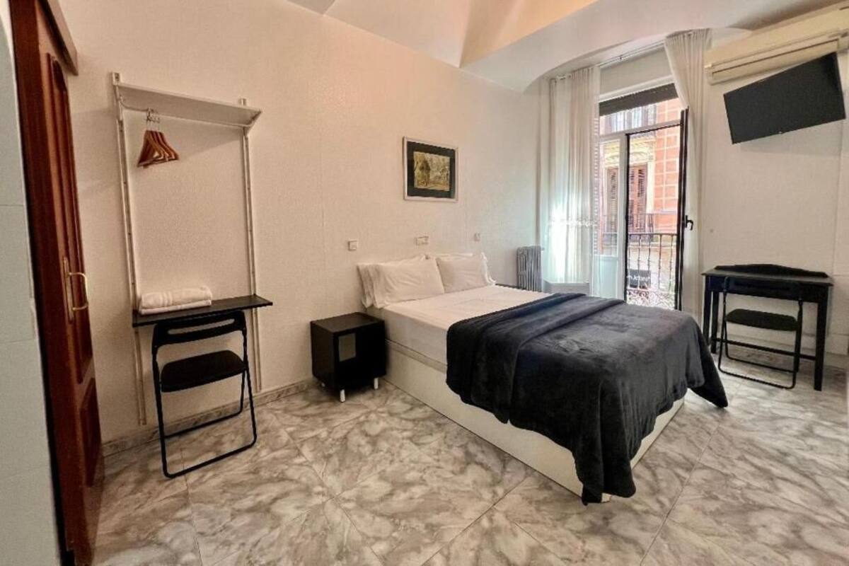 A bedroom with a bed, a small table, a hanging rack, and a window with a view.