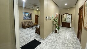 A hotel lobby with a marble floor, a sofa, a coffee table, a plant, and a ceiling fan.