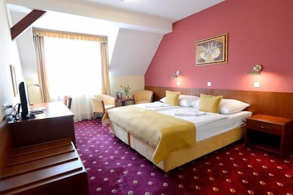 A hotel room with a bed, bedside table, desk with a computer, and a chair.