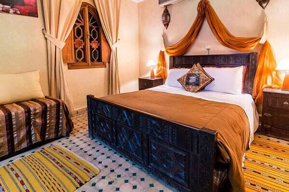 Une chambre traditionnelle avec un lit, des rideaux, une fenêtre et un tapis à motifs.