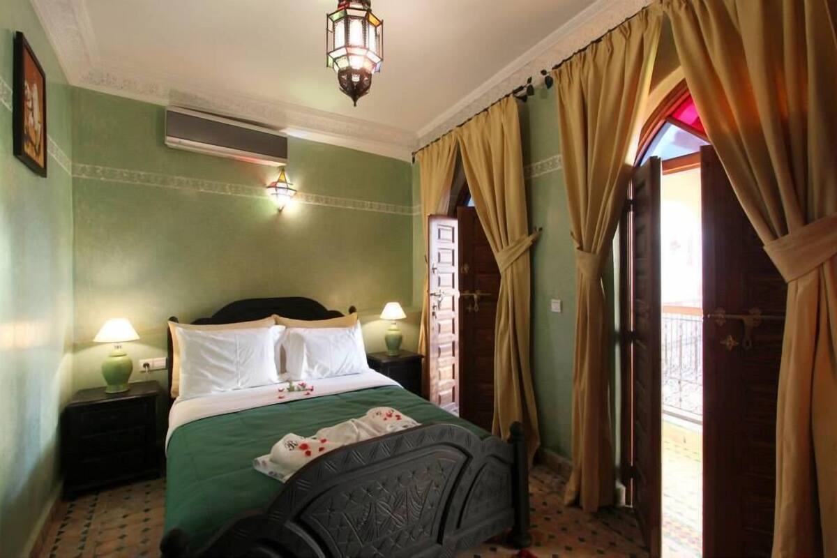 Une chambre à coucher bien rangée, avec un lit, deux lampes de chevet, une fenêtre avec des rideaux et une porte donnant sur un espace extérieur.